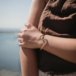 Златиста гривна Wave с 18К златно покритие, носена на ръка, идеален аксесоар за лятото.