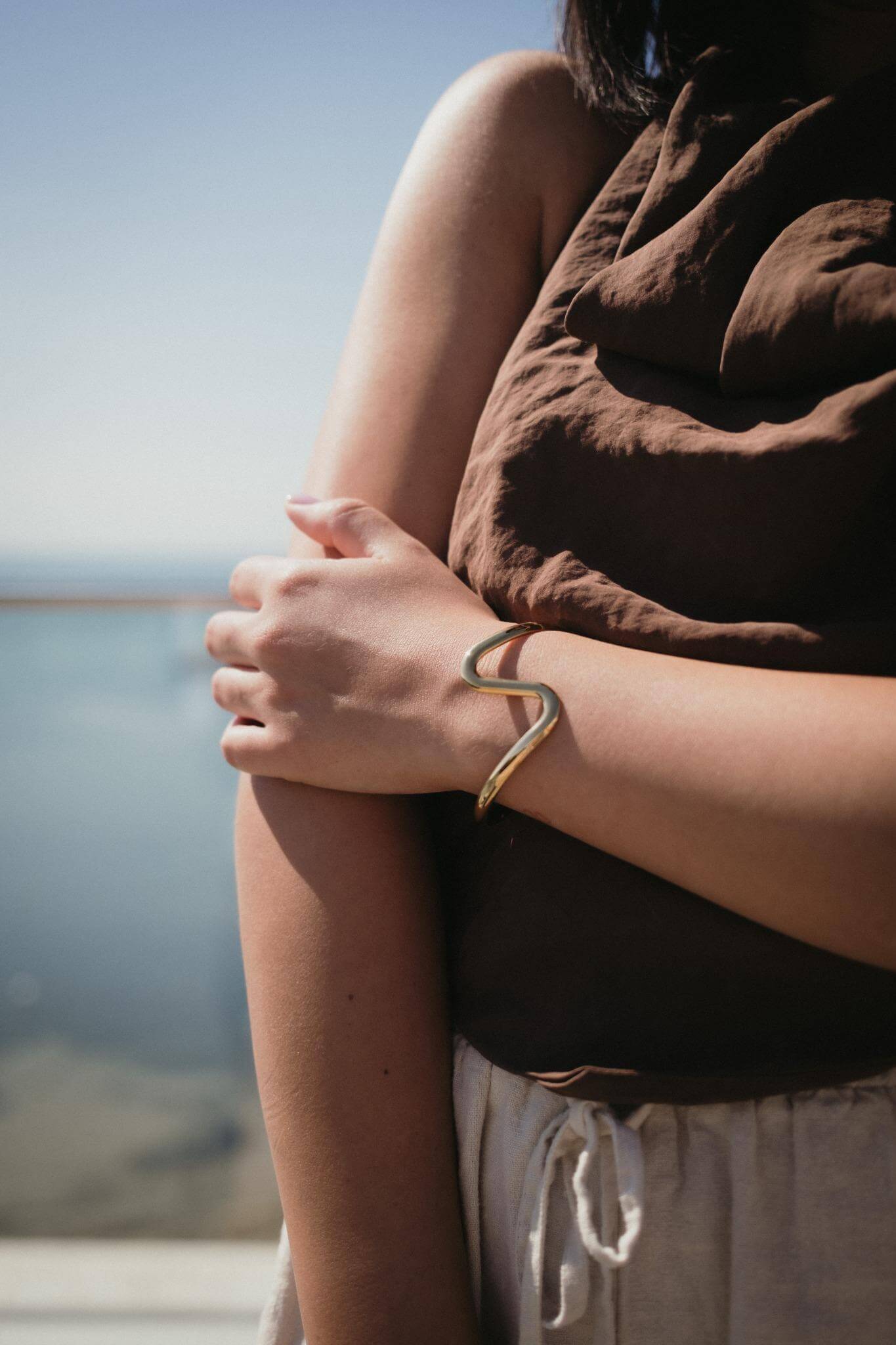 Златиста гривна Wave с 18К златно покритие, носена на ръка, идеален аксесоар за лятото.