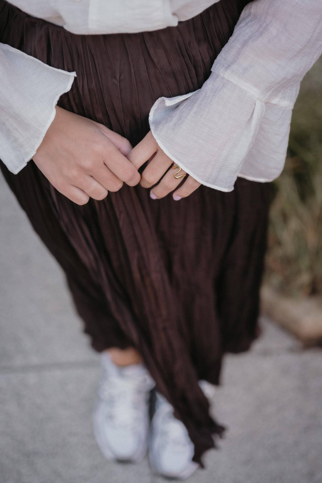 стилна жена с златист пръстен Wave и кремава риза, носеща къса пола на улицата