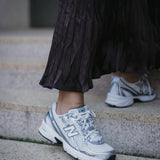 Нови спортни обувки New Balance в комбинация с дълга, plisирана пола, стъпала на стълби.