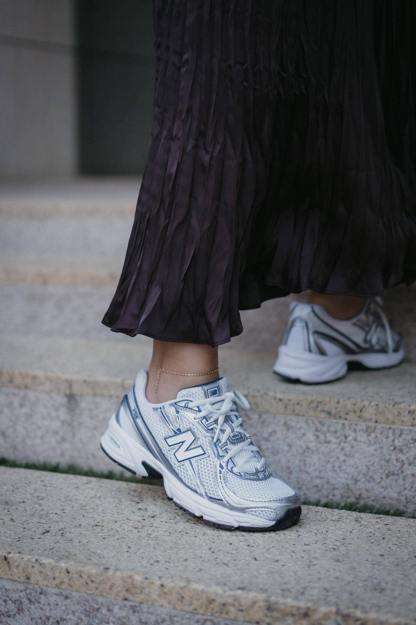 Нови спортни обувки New Balance в комбинация с дълга, plisирана пола, стъпала на стълби.