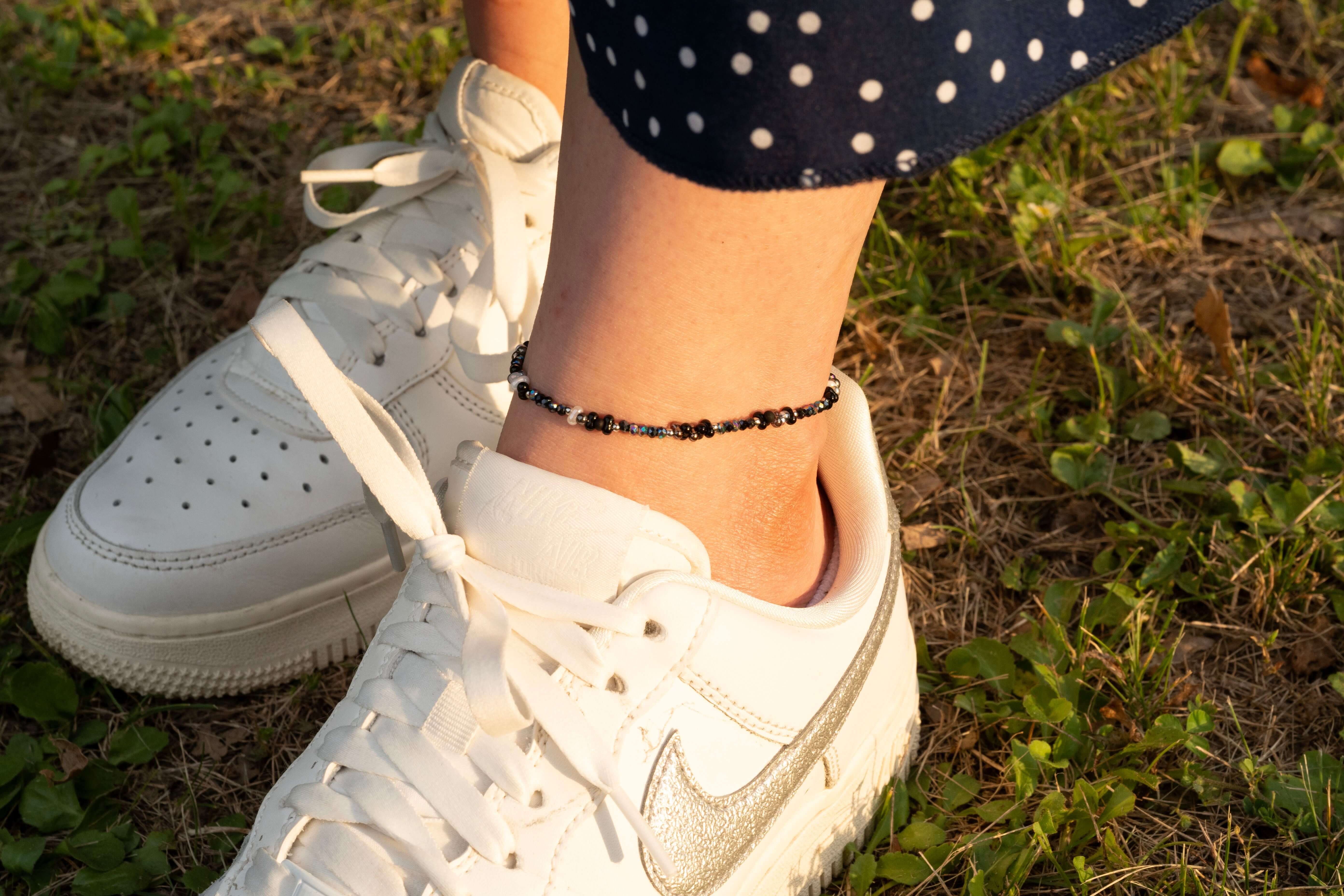 Ръчно изработена гривна за глезен с цветни мъниста, съчетана с бели спортни обувки на зелена трева.