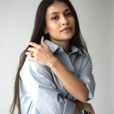 Млада жена с дълга коса носи chunky пръстен с 18К златно покритие, облечена в светлосиня риза.