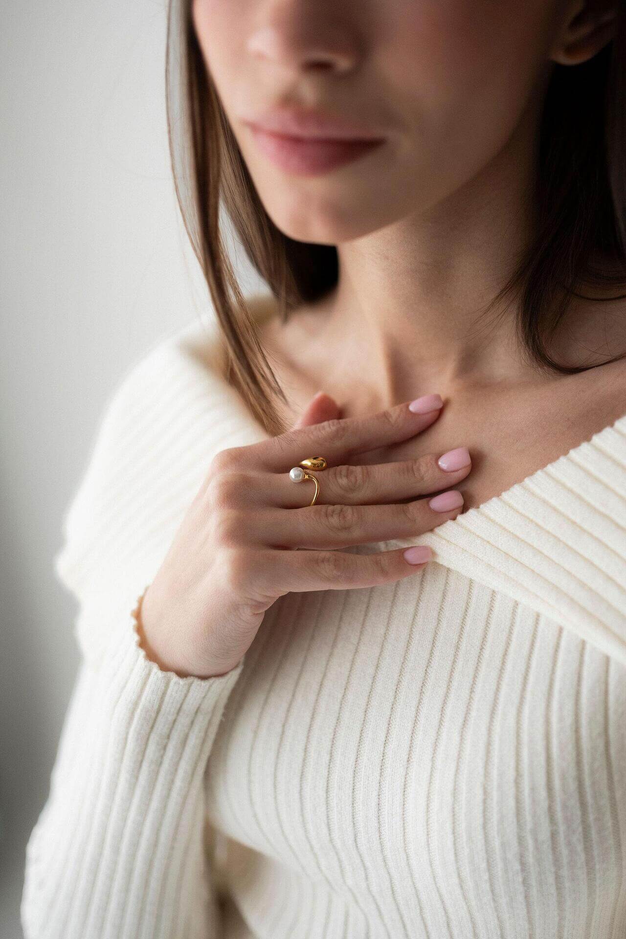 Elegant woman wearing a pearl ring with 18K gold plating, styled in a cozy white sweater.