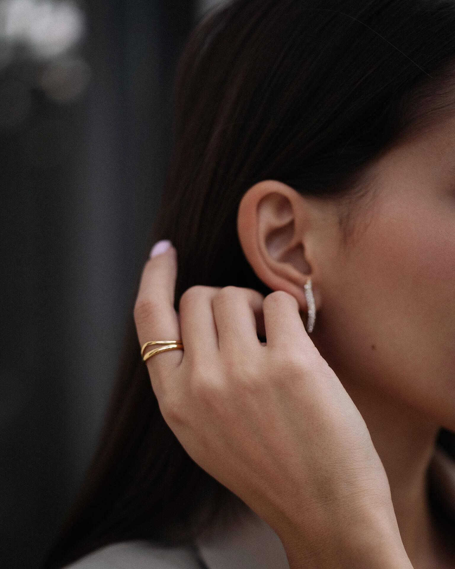 Жена с медна коса, носеща златист пръстен Liberta с 18К златно покритие и обеци.